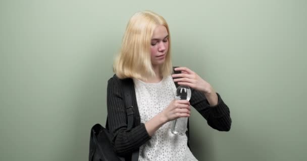 Młody student nastolatek dziewczyna z plecakiem gospodarstwa i wody pitnej z butelki na jasnozielonym tle — Wideo stockowe