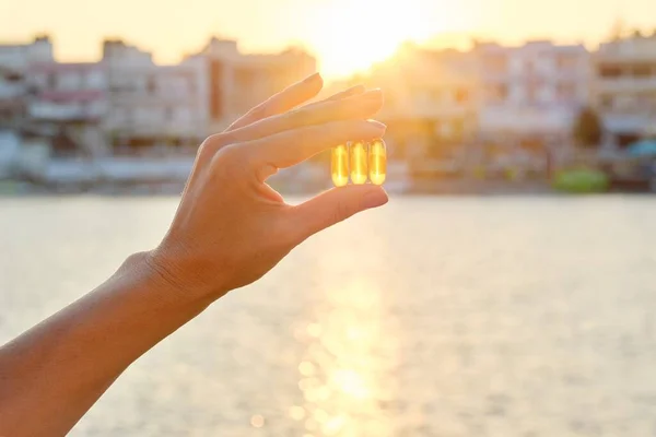 Cápsula de gel amarillo vitamina d omega-3 en la mano de las mujeres, fondo de mar sol — Foto de Stock