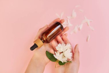 Çiçekli kadın elleri ve şişede kozmetik ürünler, pembe arka plan