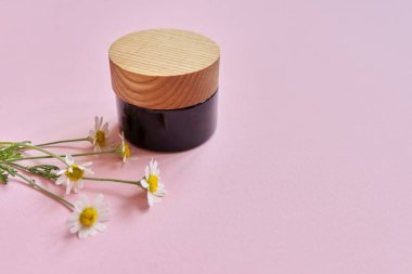 Şişe içinde kozmetik ürünü, pembe arka planda papatya çiçekleri.