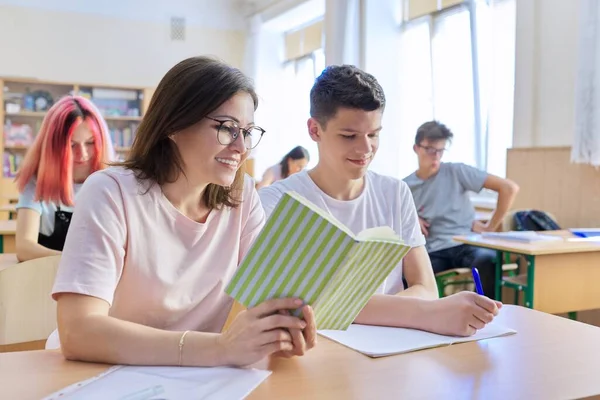 Medelålders kvinnolärare sitter vid skrivbordet med tonårsstudent undervisar — Stockfoto