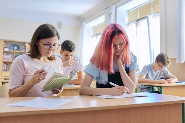 Profesora de mediana edad sentada en el escritorio con estudiantes adolescentes enseña —  Fotos de Stock