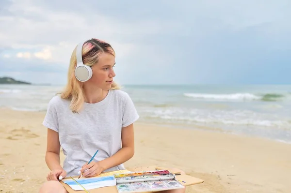 Young woman artist painting with watercolors sitting on the seashore