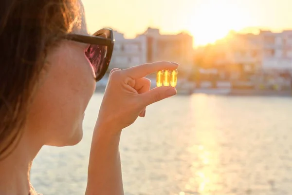 Cápsula de gel amarillo vitamina d omega-3 en la mano de las mujeres, fondo de mar sol — Foto de Stock