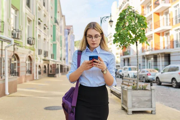 Young business woman with smartphone walking along city street — Stock Photo, Image