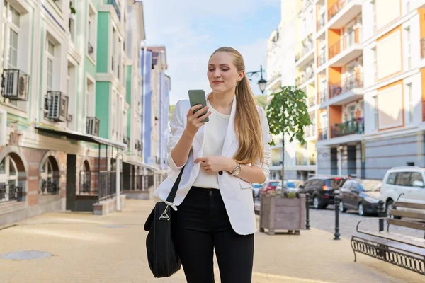 Young business woman with smartphone walking along city street — Stock Photo, Image