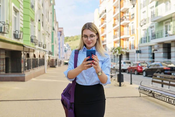 Молодая деловая женщина со смартфоном прогуливается по городской улице — стоковое фото