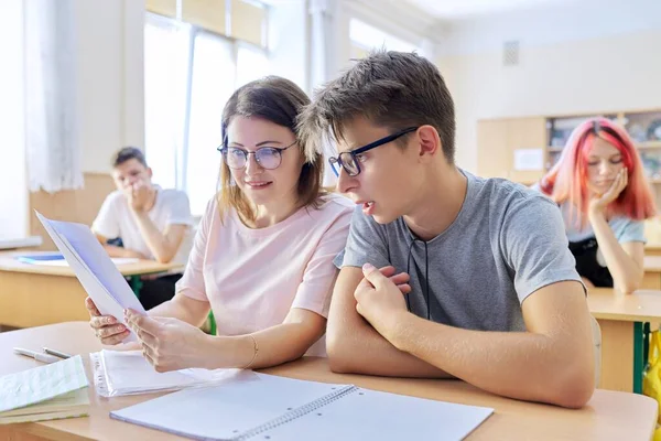 Profesora de mediana edad sentada en el escritorio con estudiantes adolescentes enseña —  Fotos de Stock