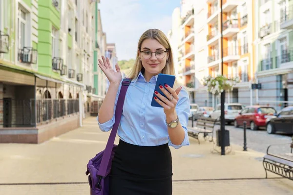 Business woman in glasses in blue shirt with laptop bag using smartphone — Stock Photo, Image