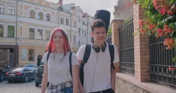 Trendy teenage hipsters boy and girl walking talking on city street, boy with guitar in case — Stock Video