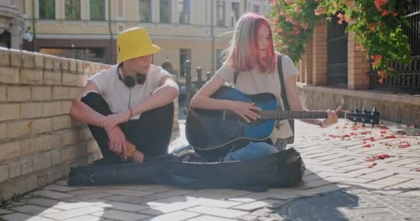 Laki-laki dan gadis remaja dengan gitar akustik di jalan kota, gadis bermain gitar bernyanyi dengan teman — Stok Video