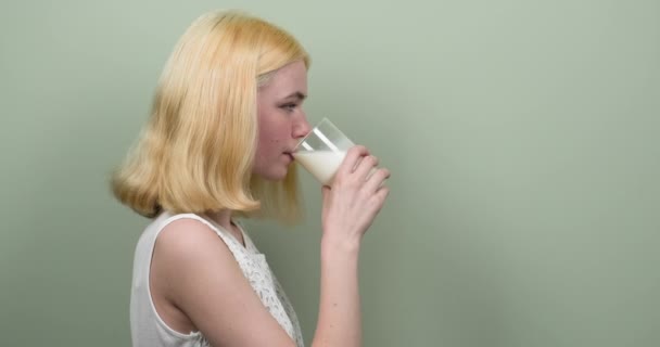 Adolescente blonde buvant du lait à partir de verre sur fond vert clair. Alimentation saine, nutrition, jeunesse, concept de personnes — Video