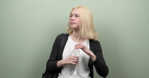 Ung student tonåring flicka med ryggsäck innehav och dricksvatten från flaska på ljusgrön bakgrund — Stockvideo