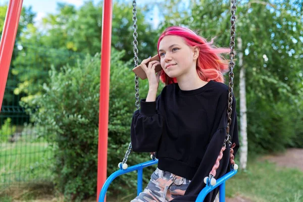 Chica adolescente de moda con el pelo teñido con teléfono inteligente montar en el columpio —  Fotos de Stock