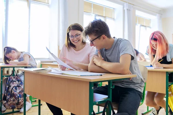 Урок в классе старшеклассников, учительница, сидящая за столом с ученицей — стоковое фото