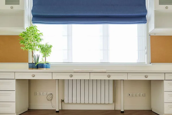 Interior of room, workplace near window, furniture, desk, blue roman blind, wall shelves