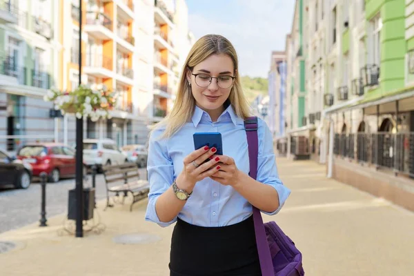 Business woman in glasses in blue shirt with laptop bag using smartphone — Stock Photo, Image