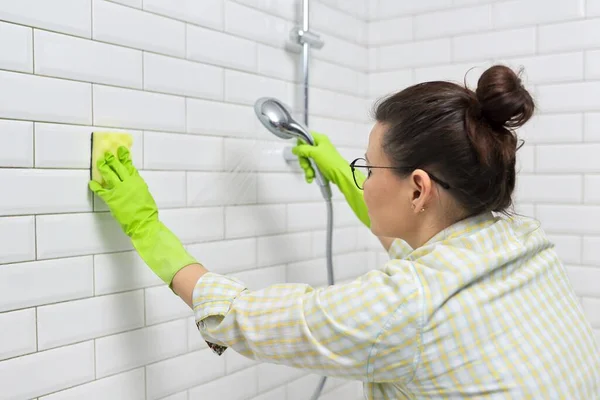 Schoonmaken van de badkamer, vrouw wassen tegelwand met washandje met wasmiddel — Stockfoto