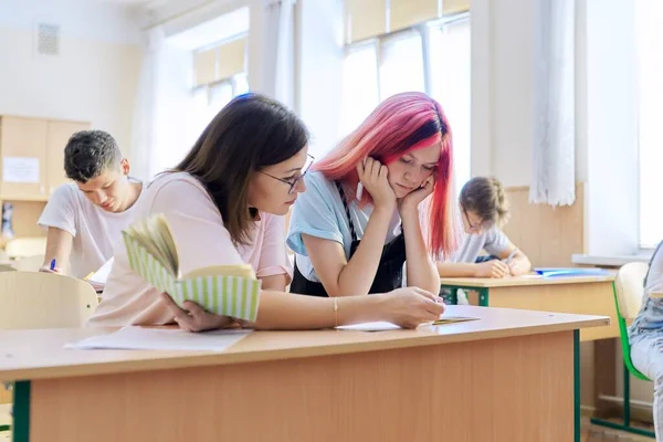 Lekcja w klasie licealistów, nauczycielka siedząca przy biurku z uczennicą — Zdjęcie stockowe