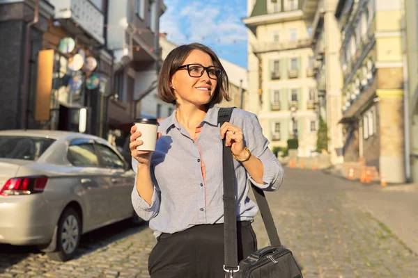 Mature business woman in glasses with office laptop bag walking along city street — Stock Photo, Image