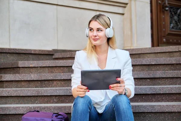 Young woman in headphones with digital tablet relaxing sitting on steps in city — Stock Photo, Image