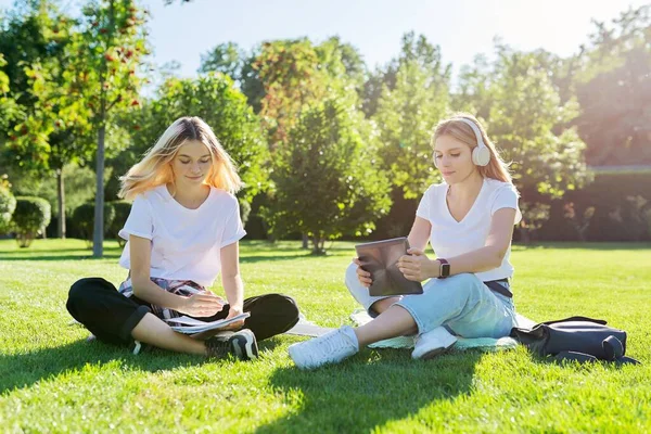 Lányok tizenéves diákok ül zöld gyep a parkban hátizsák, digitális tabletta — Stock Fotó