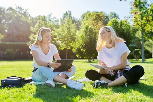 Девочки подростки сидят на зеленой лужайке в парке с рюкзаком, цифровой планшет — стоковое фото