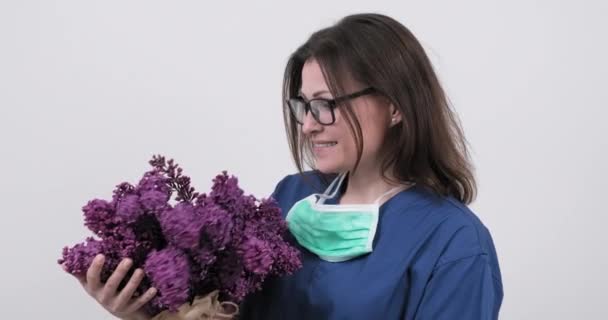 Retrato de médico fêmea sorridente maduro em óculos com máscara médica protetora segurando buquê de flores — Vídeo de Stock