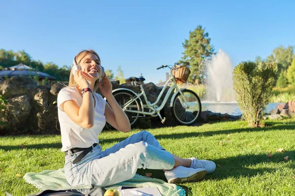 Outdoor portrait of young happy woman in headphones, listening to music