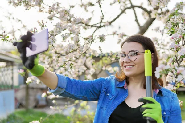 Happy woman in blooming garden taking selfie photo on smartphone