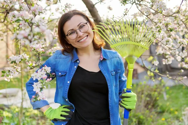 Spring gardening, portrait of mature smiling woman with rake looking at camera