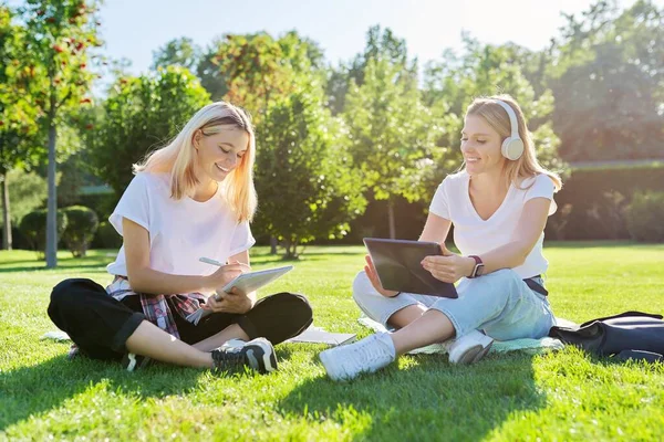 Chicas adolescentes estudiantes sentados en el césped verde en el parque con mochila, tableta digital — Foto de Stock