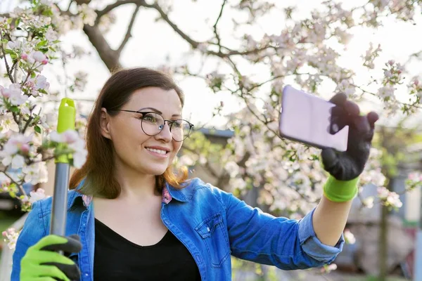 Happy woman in blooming garden taking selfie photo on smartphone