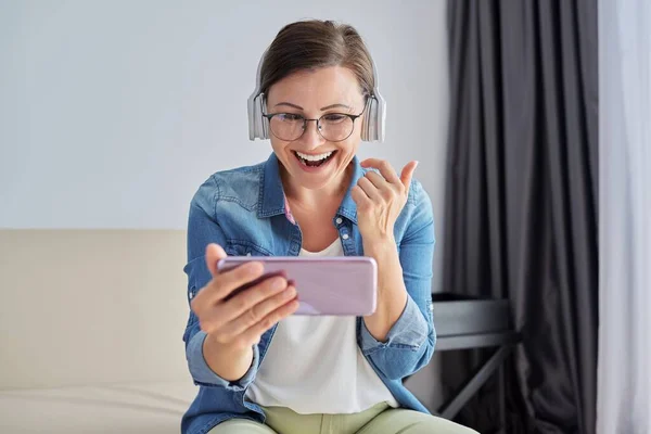 Maturo positivo parlando donna in cuffia guardando lo schermo dello smartphone, videochiamata — Foto Stock