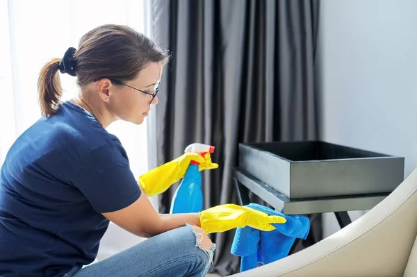 Limpieza de la casa, mujer en guantes con un trapo y spray limpiando el polvo y puliendo muebles —  Fotos de Stock