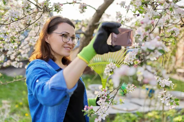 Счастливая женщина в цветущем саду делает селфи фото на смартфоне — стоковое фото