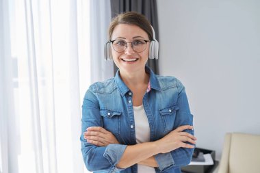 Gözlük ve kulaklık takan kendinden emin orta yaşlı bir kadının portresi.