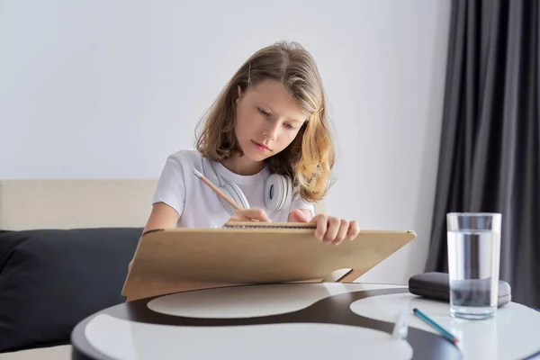 Meisje kind student zit op de bank aan het bureau tekenen en schrijven met potlood — Stockfoto