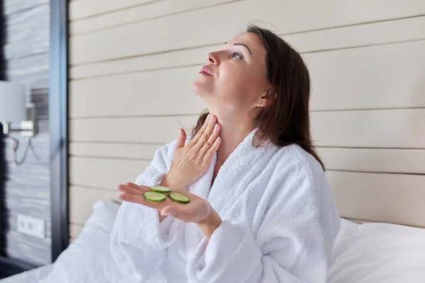 Mulher madura em roupão de banho fazendo tratamentos de spa em casa com pepinos — Fotografia de Stock