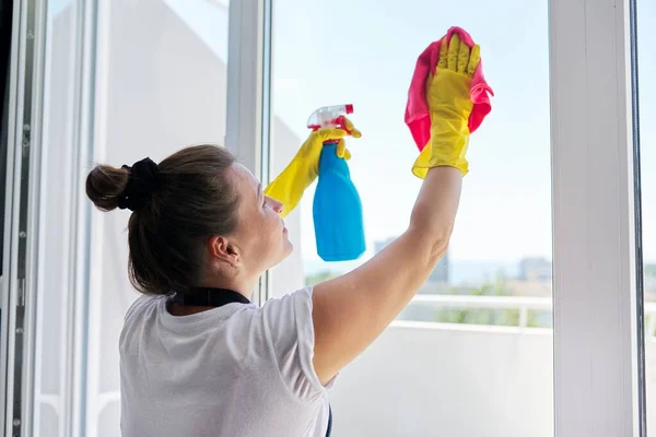 House cleaning, mature woman in rubber gloves wearing an apron washing windows — Stock Photo, Image