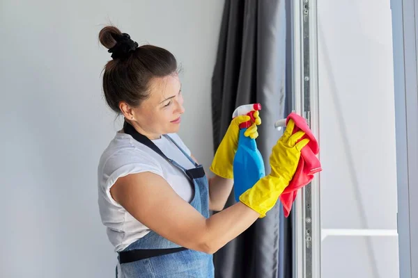 Putzfrau, reife Frau in Gummihandschuhen, die eine Schürze trägt und Fenster wäscht — Stockfoto