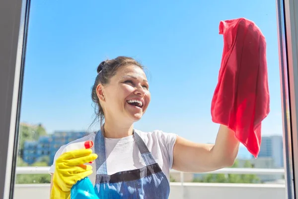 Putzfrau, reife Frau in Gummihandschuhen, die eine Schürze trägt und Fenster wäscht — Stockfoto