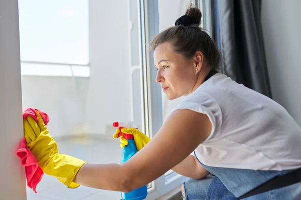 Pulizia della casa, donna matura in guanti di gomma che indossa un grembiule lavare le finestre — Foto Stock