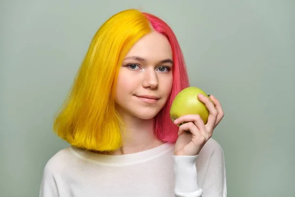 Huvudskott av en vacker tonåring flicka med ett äpple på en grön bakgrund — Stockfoto