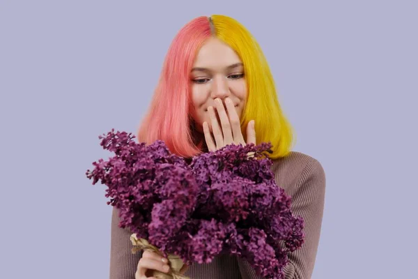 Överraskad tonåring flicka med färgat rosa gult hår håller lila blommor i händerna — Stockfoto