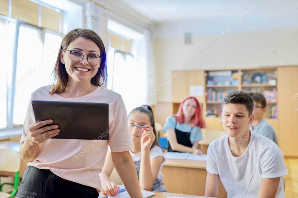 Portrait of female teacher at school, smiling woman in glasses with digital tablet
