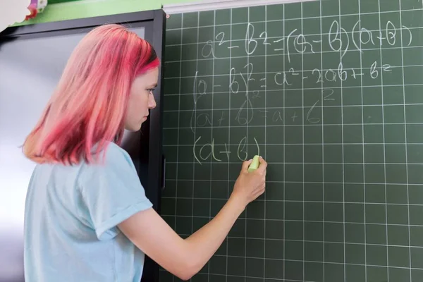 Adolescente estudiante en una lección de matemáticas escribiendo con tiza en una pizarra — Foto de Stock