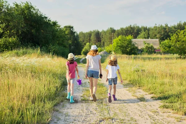 Verano, naturaleza, niños. Tres chicas caminando con la espalda en un camino rural — Foto de Stock
