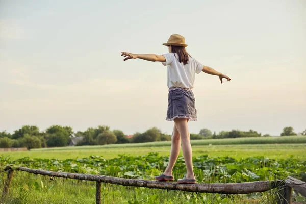 Lato, przyroda, szczęście, koncepcja dzieciństwa. Dziewczyna w kapeluszu spaceruje po drewnianym ogrodzeniu — Zdjęcie stockowe