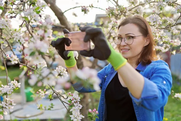 Happy woman in blooming garden taking selfie photo on smartphone